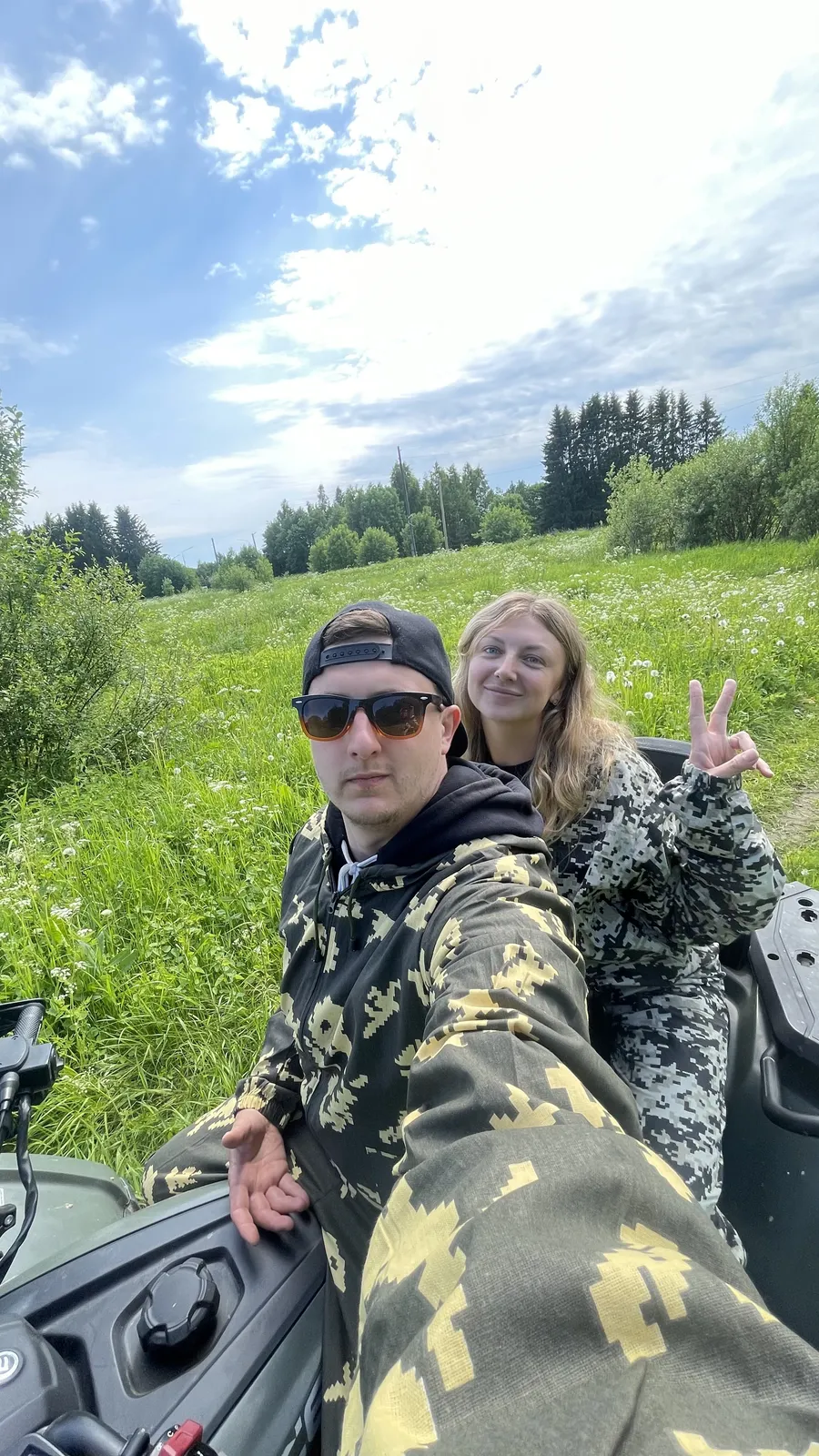 Селфи пары в камуфляже на квадроцикле посреди летнего луга